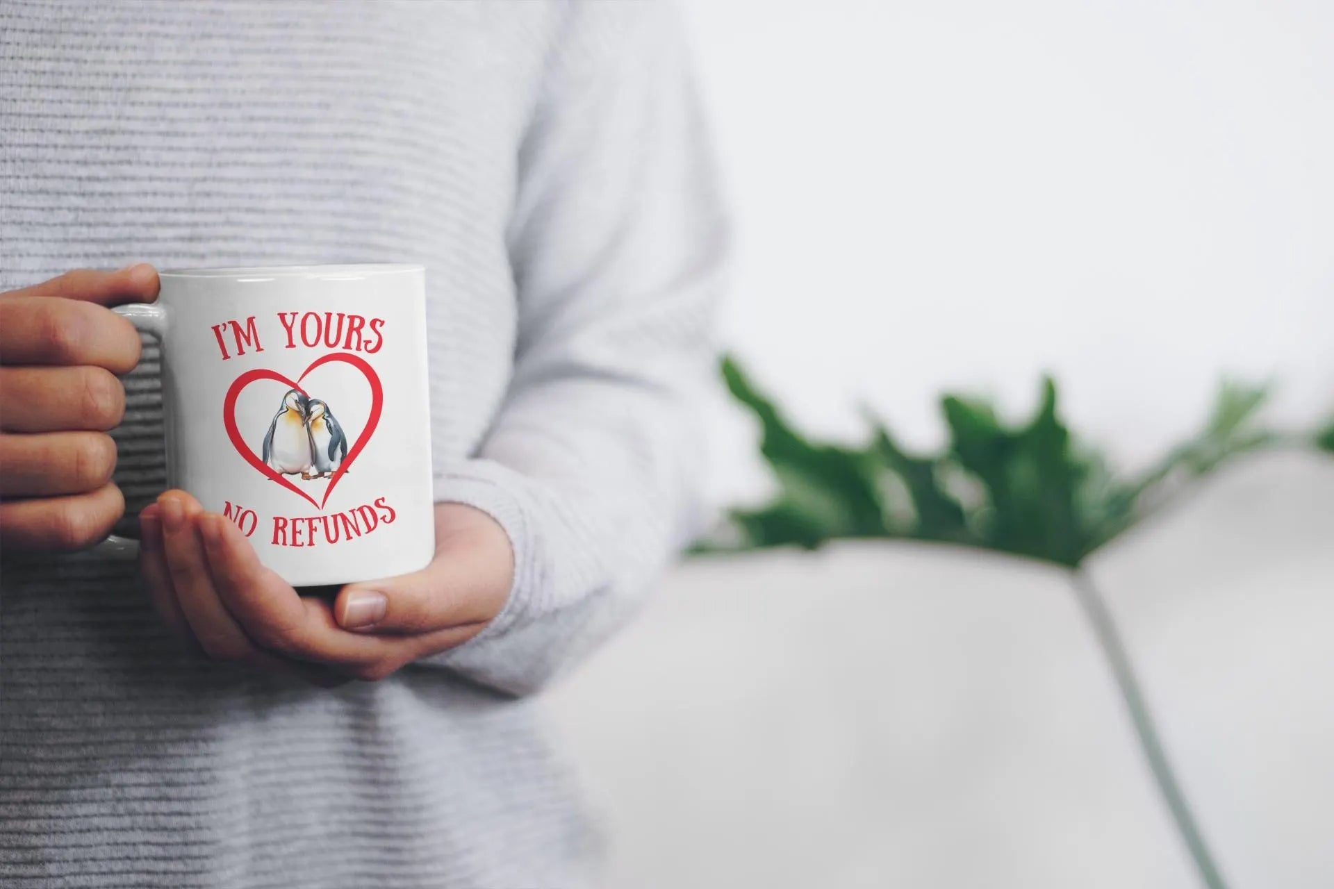 Person holding a mug with penguins and text, blurred background