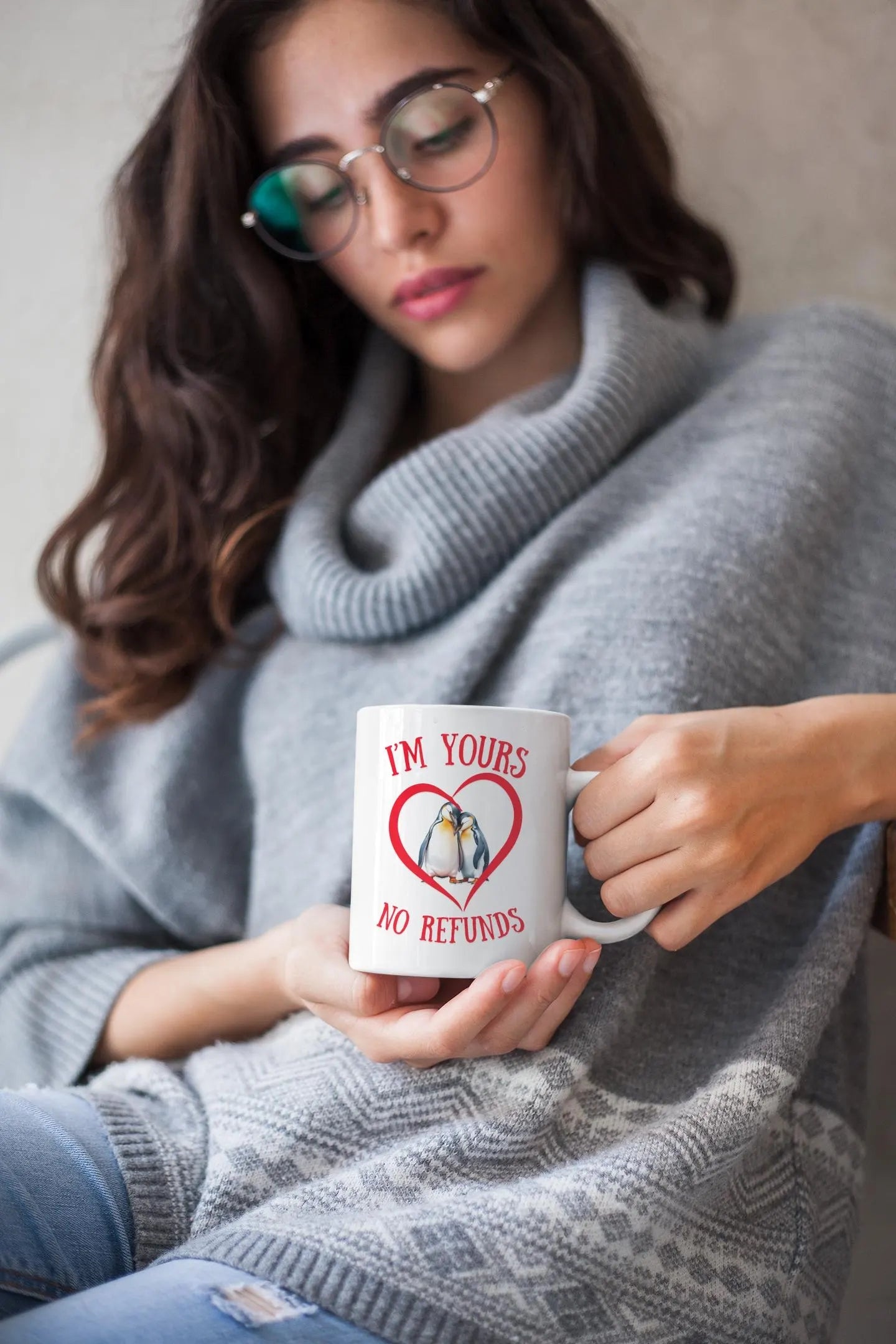 Woman holding a mug with a heart design and text, wearing a gray sweater.