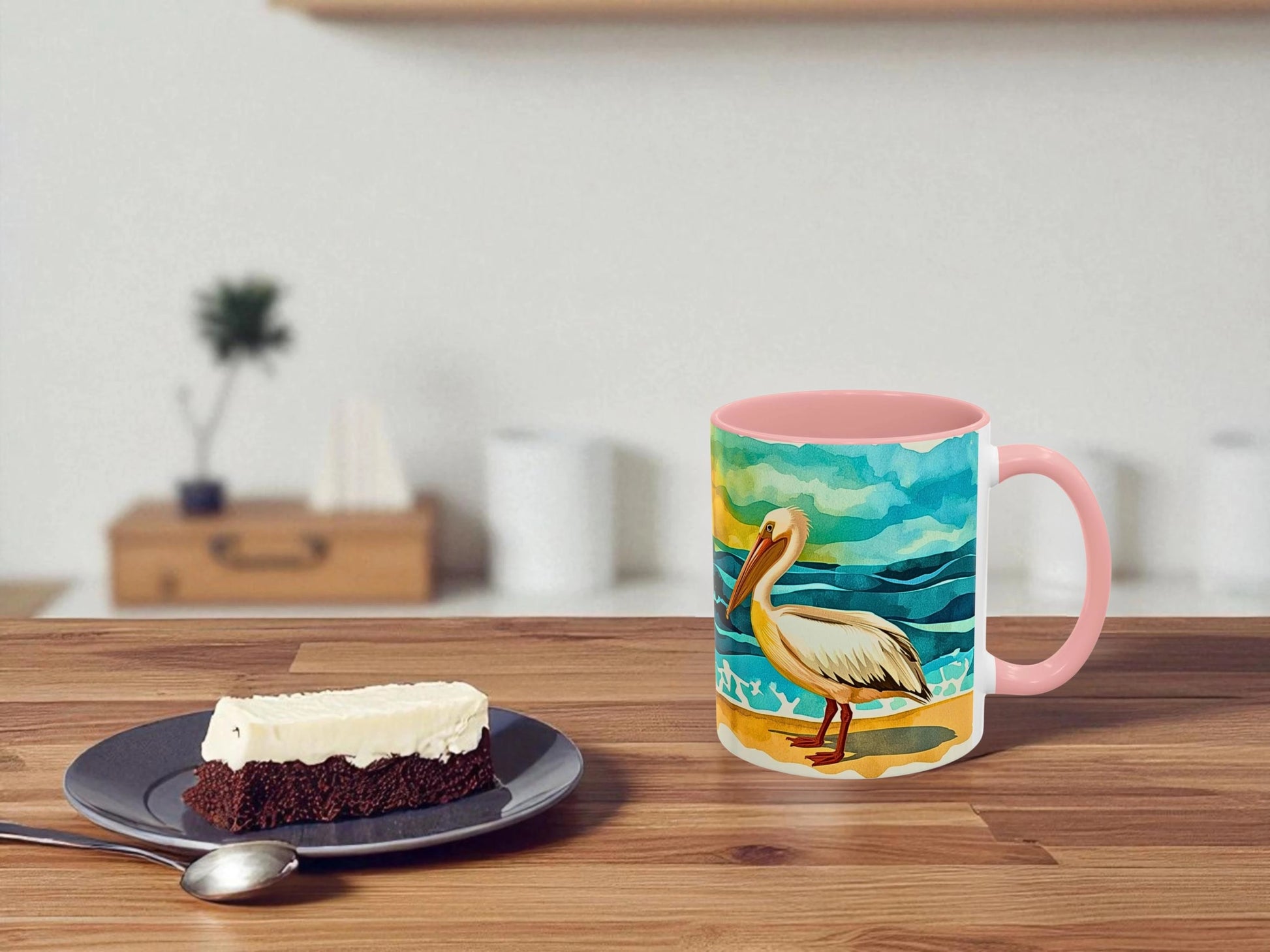 Mug with a pelican design on a wooden table next to a slice of cake.