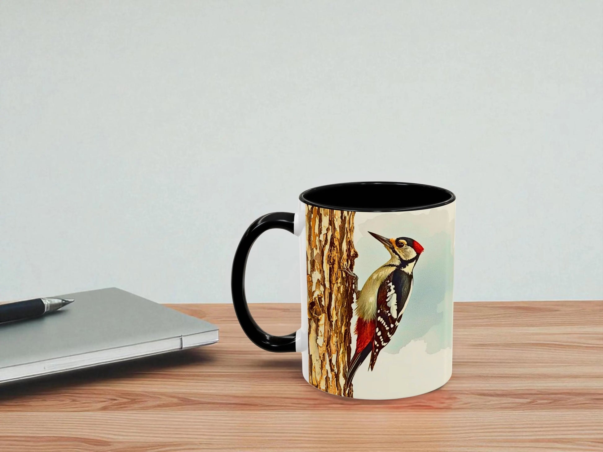 Mug with a bird design on a wooden table next to a laptop.
