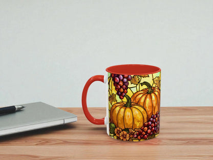 Mug with pumpkin and grape design on a wooden table next to a laptop.