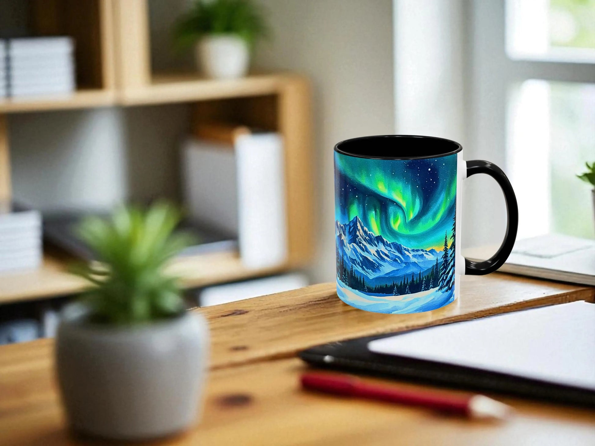 Mug with a Northern Lights design on a wooden desk with a plant and tablet in the background.