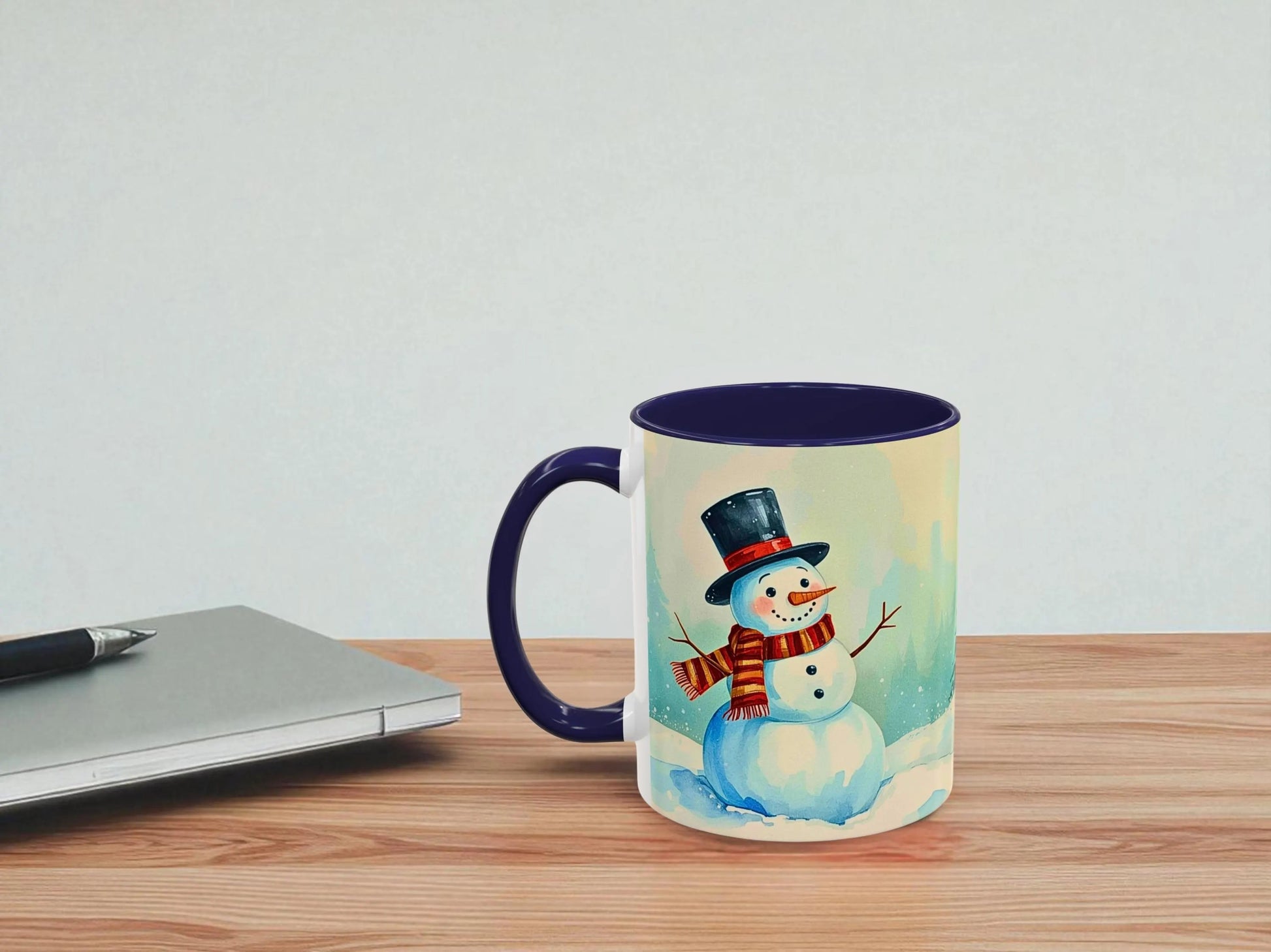 Mug with a snowman design on a wooden table next to a laptop.