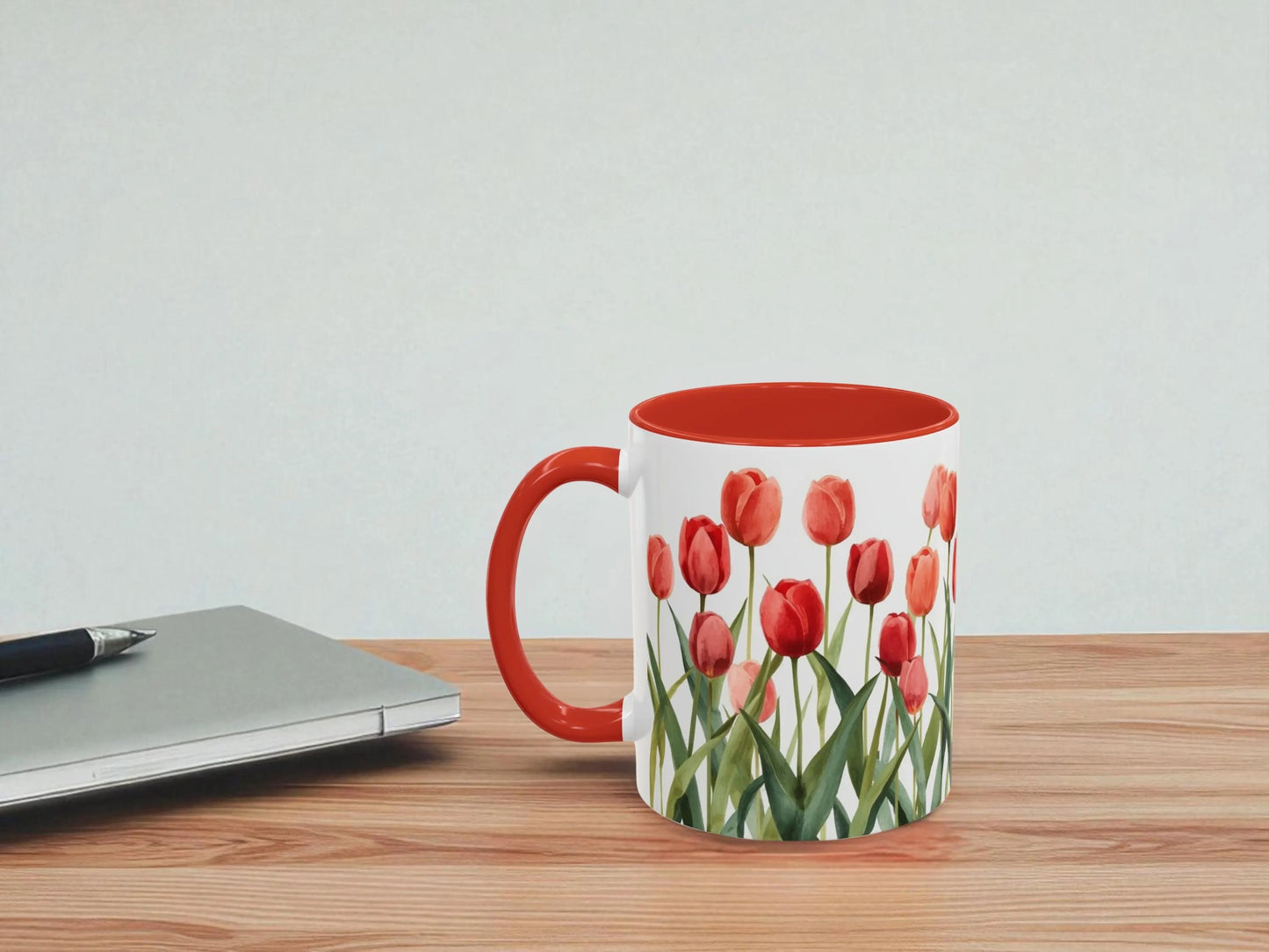 Mug with red tulip design on a wooden table next to a laptop.
