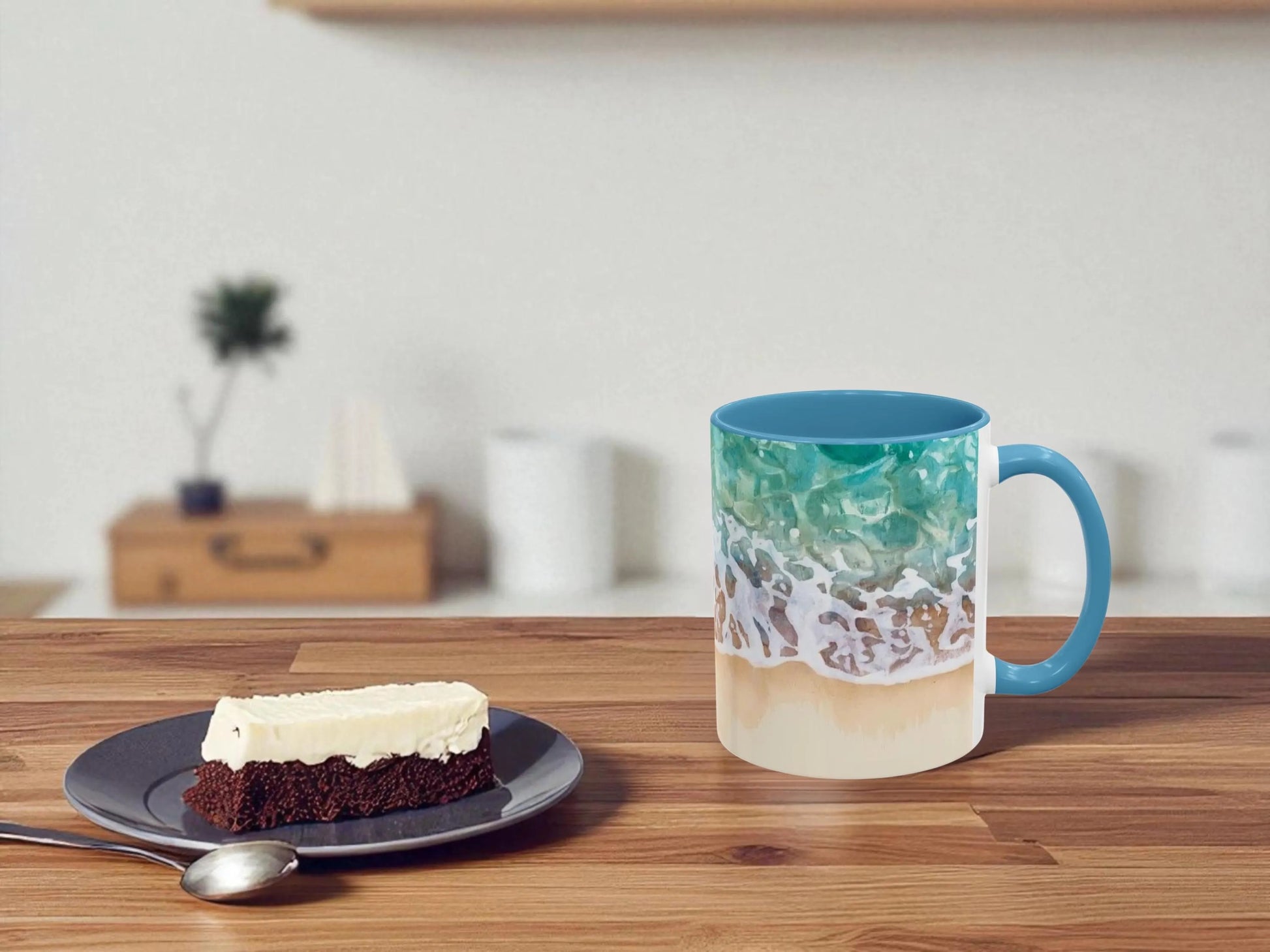 Mug with ocean design on a wooden table next to a brownie and a spoon.