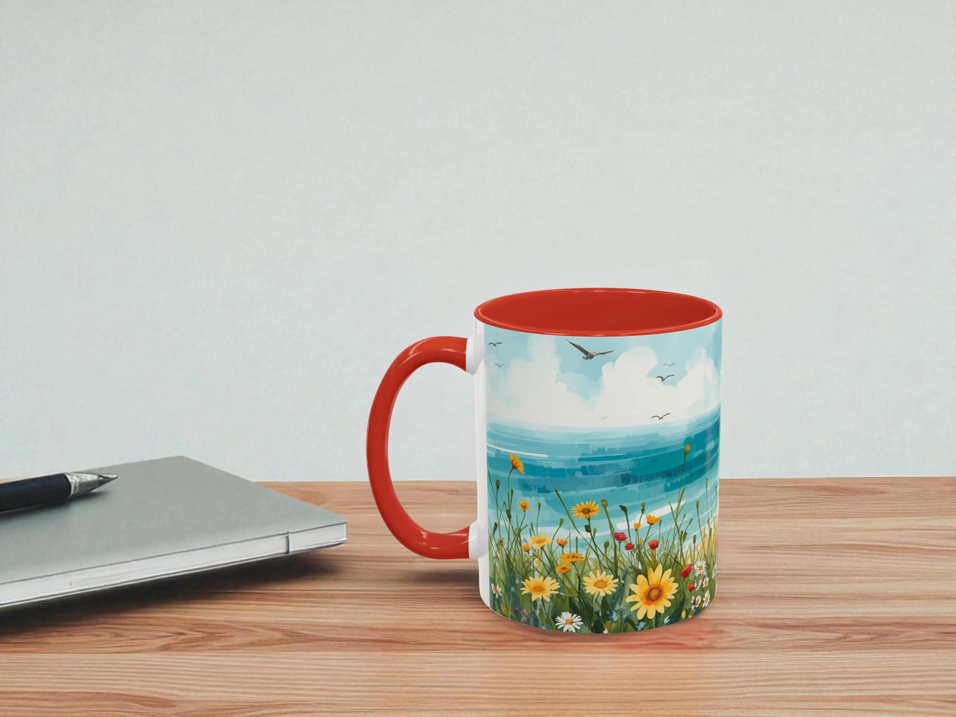 Mug with scenic design on a wooden table next to a laptop.