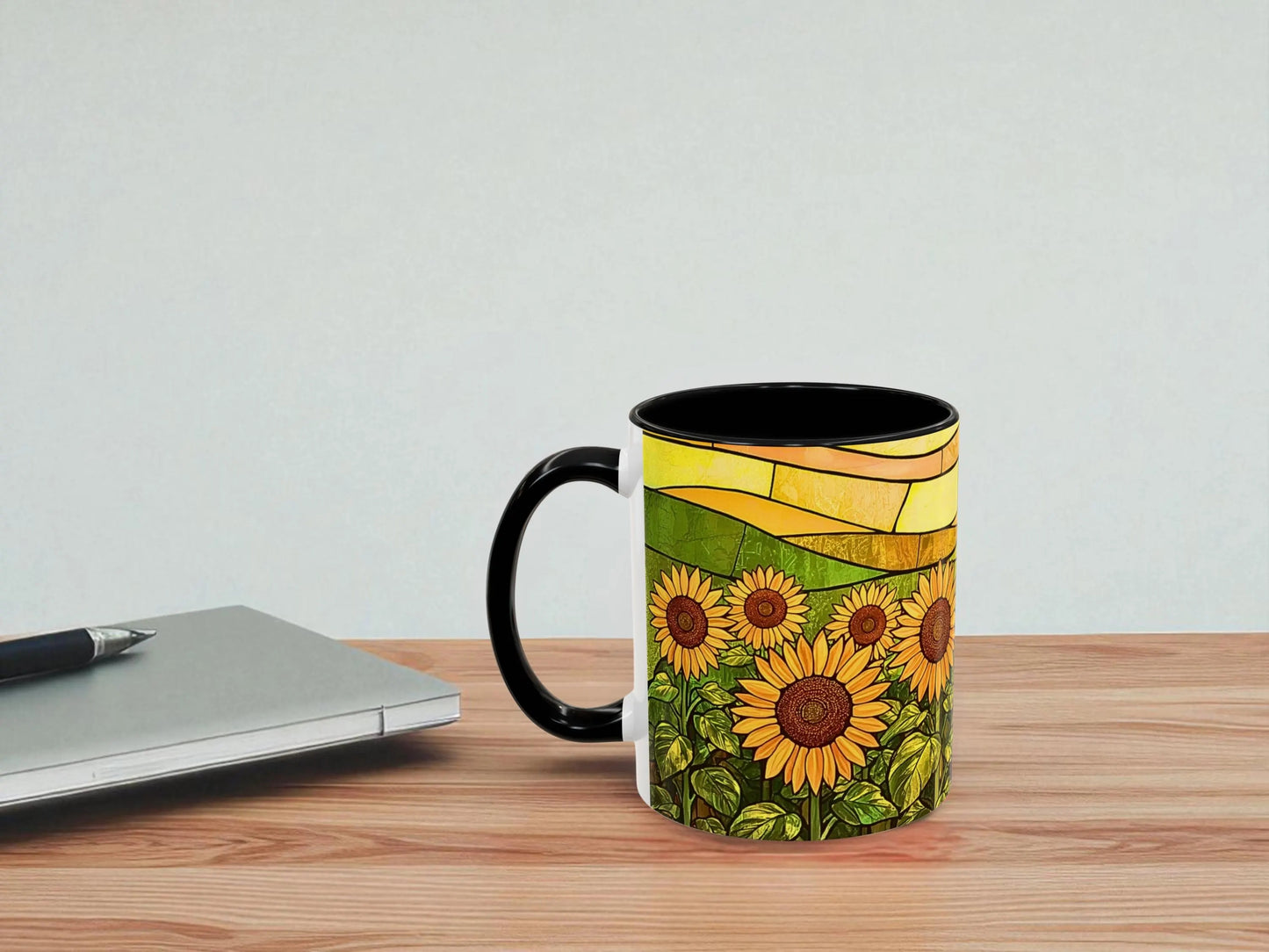 Mug with sunflower design on a wooden table next to a laptop.