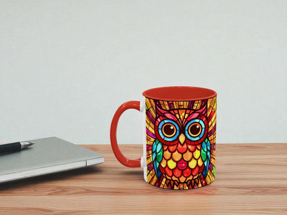 Colorful owl mug with a red handle on a wooden surface next to a laptop.