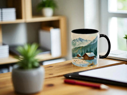 Mug with a mountain and cabin design on a desk with a laptop and plant.