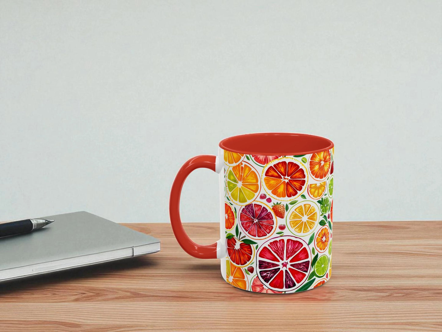 Colorful mug with citrus pattern on a wooden table next to a laptop.
