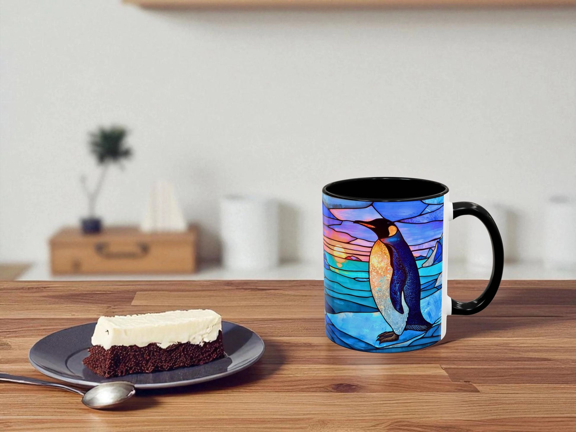 Mug with penguin design on a wooden table with a slice of cake and spoon.