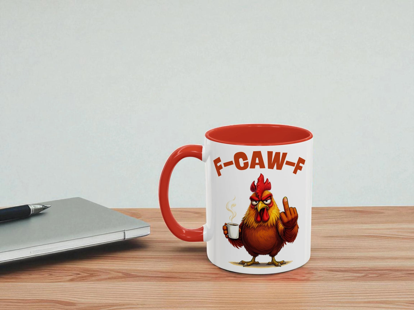 Mug with a rooster design and 'F-CAW-F' text on a wooden table with a laptop.