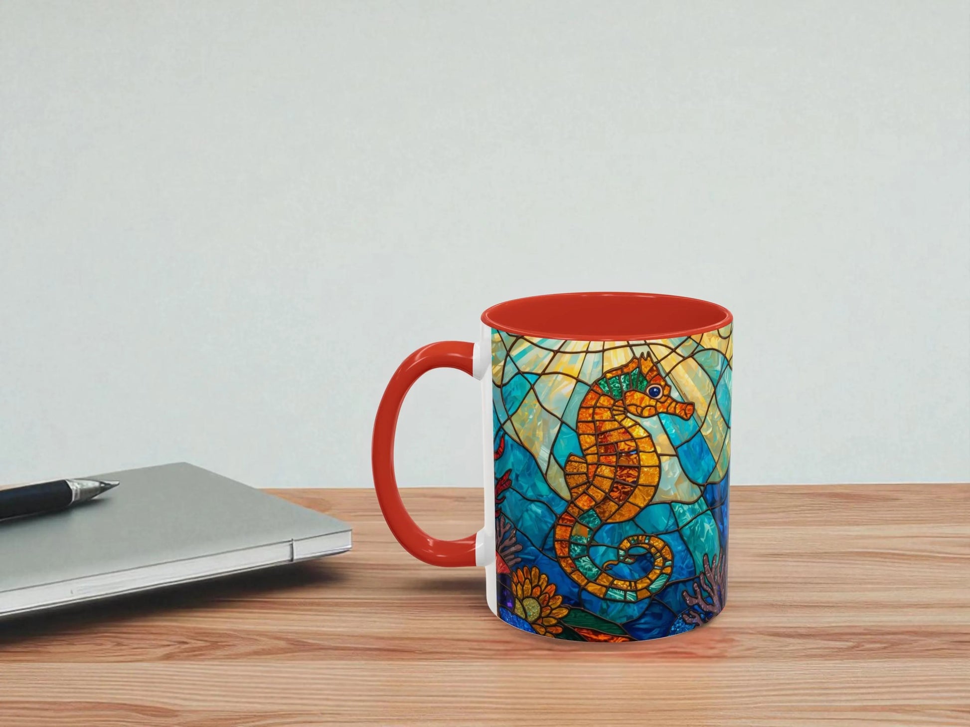 Colorful mug with seahorse design on a wooden table next to a laptop.