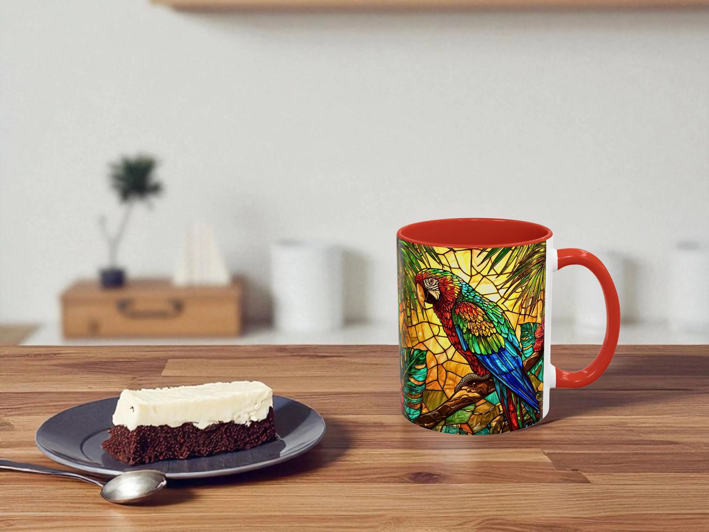 Colorful mug with parrot design on a wooden table with a slice of cake and spoon.