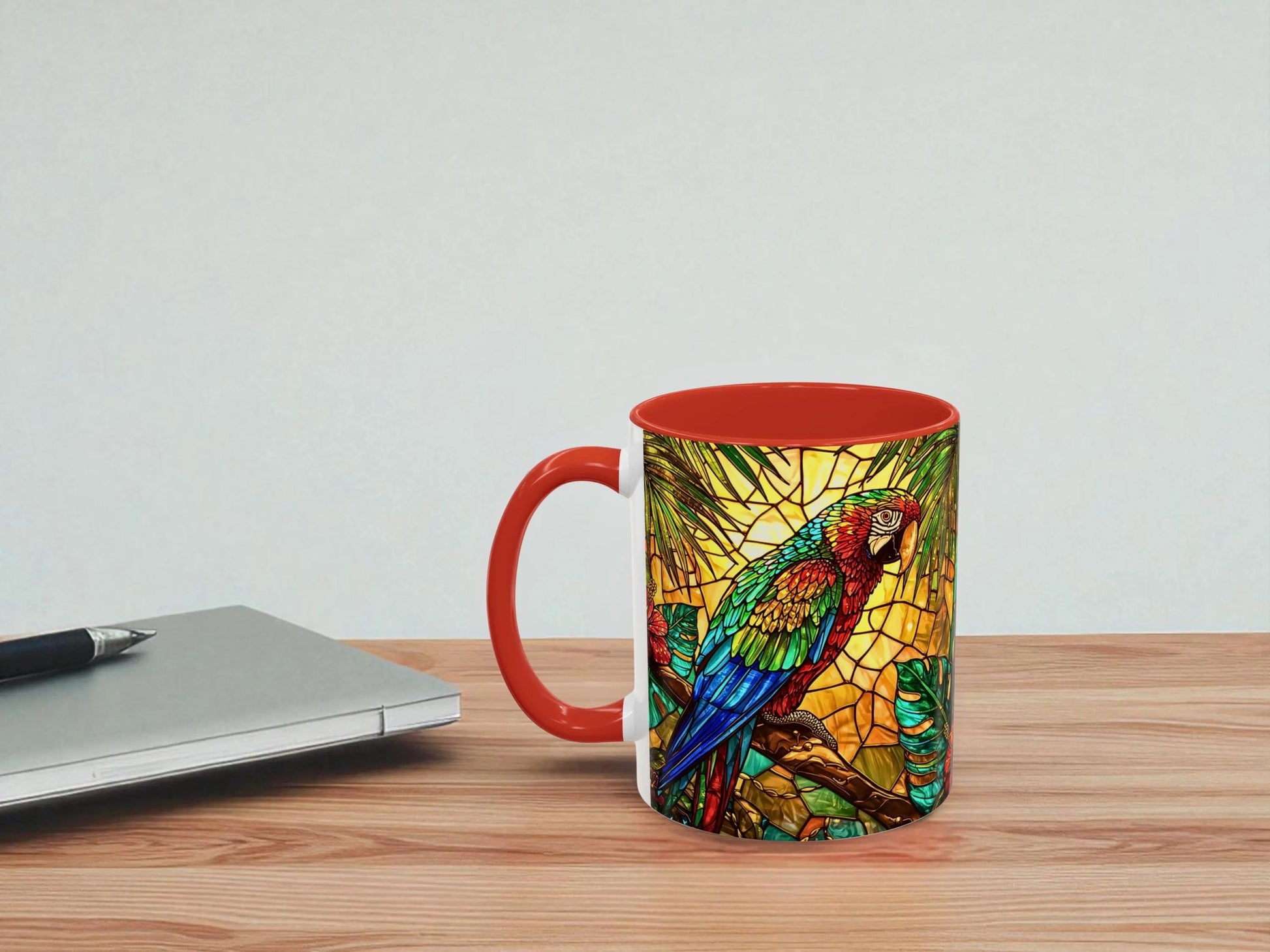 Mug with a colorful parrot design on a wooden table next to a laptop.