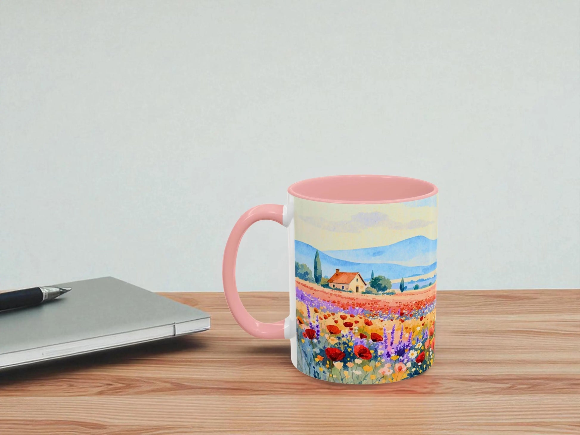 Mug with a scenic design on a wooden table next to a laptop.
