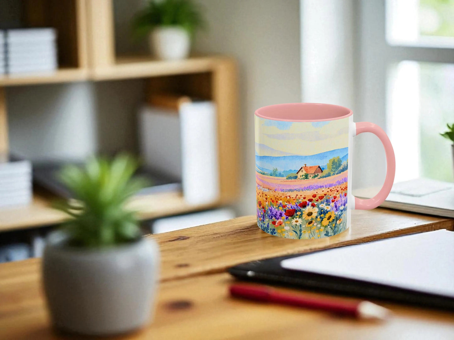 Colorful mug with a scenic design on a wooden desk, surrounded by office items.