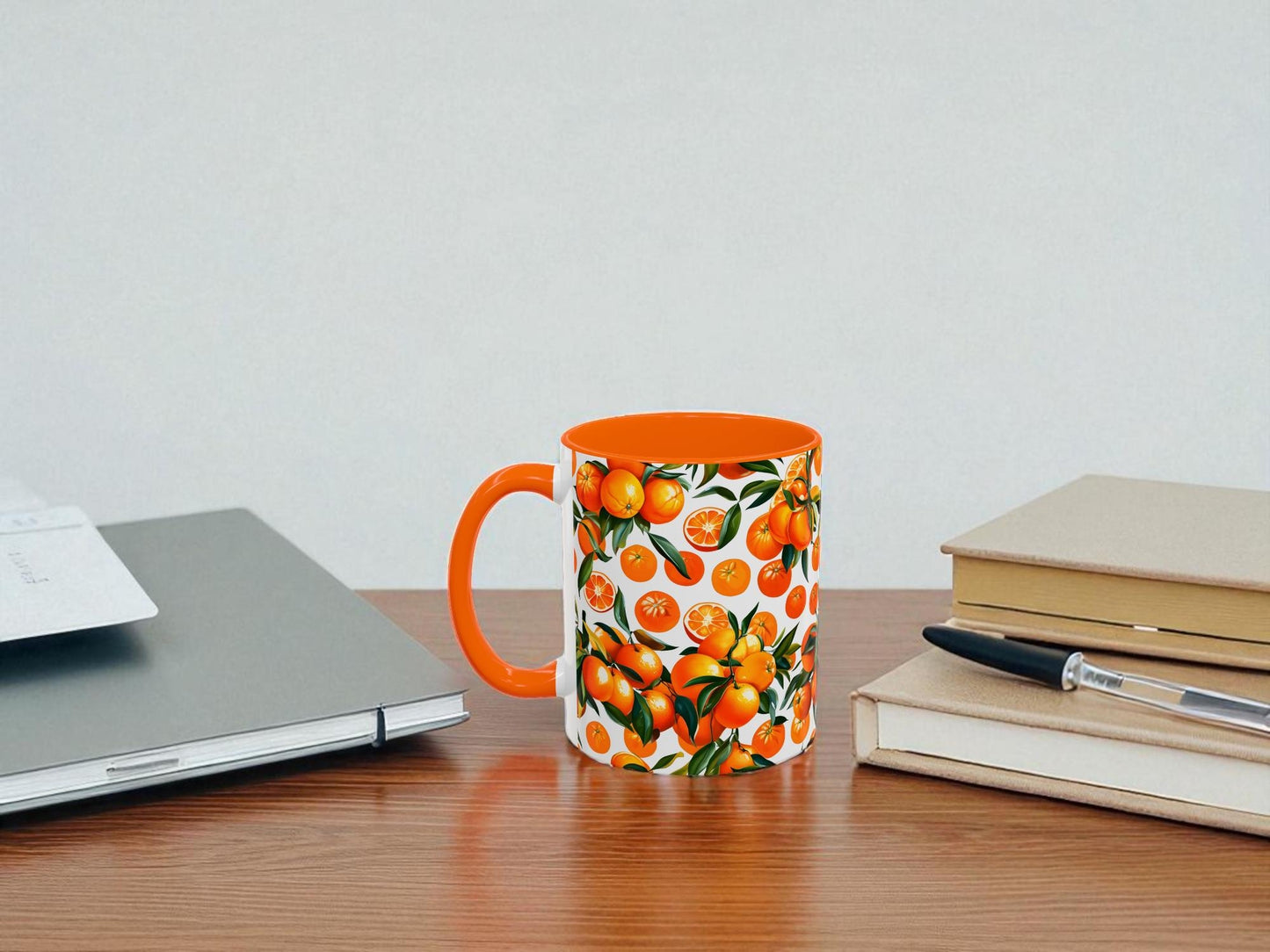 Mug with orange design on a desk next to a laptop and books