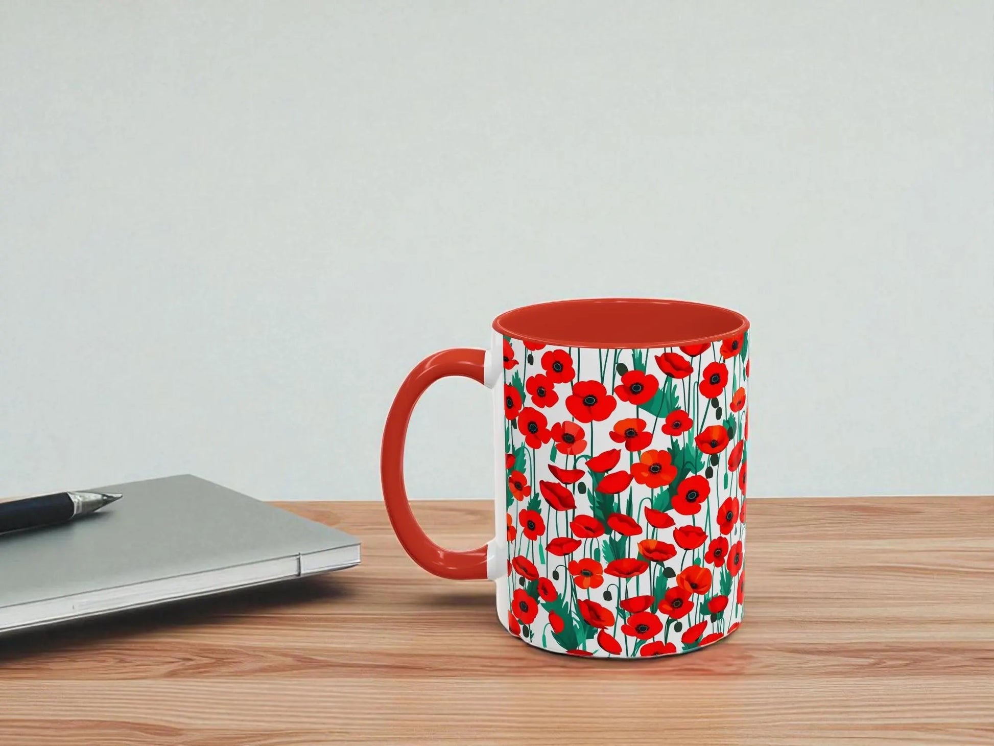 Mug with red poppy pattern on a wooden table next to a laptop.