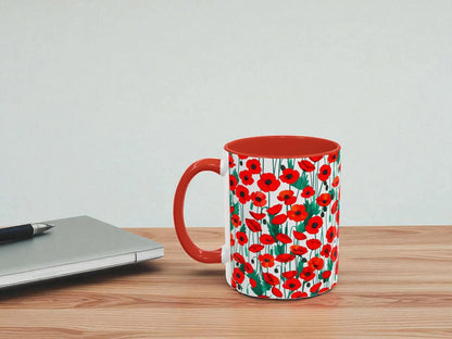 Mug with red poppy pattern on a wooden table next to a laptop.