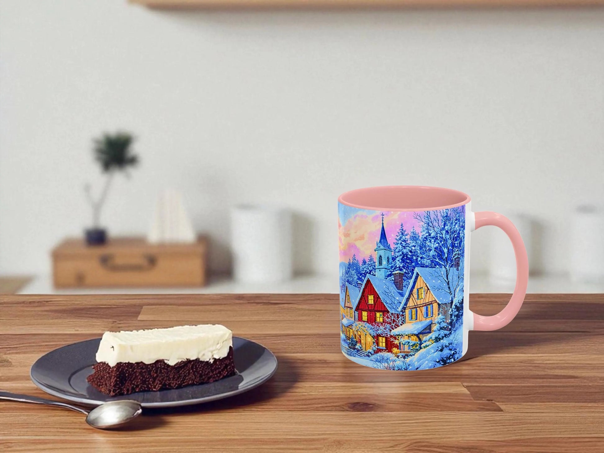 Mug with a scenic design on a wooden table next to a slice of cake.