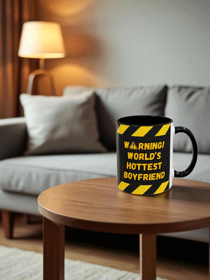 Mug with 'Warning! World's Hottest Boyfriend' text on a wooden table in a living room.
