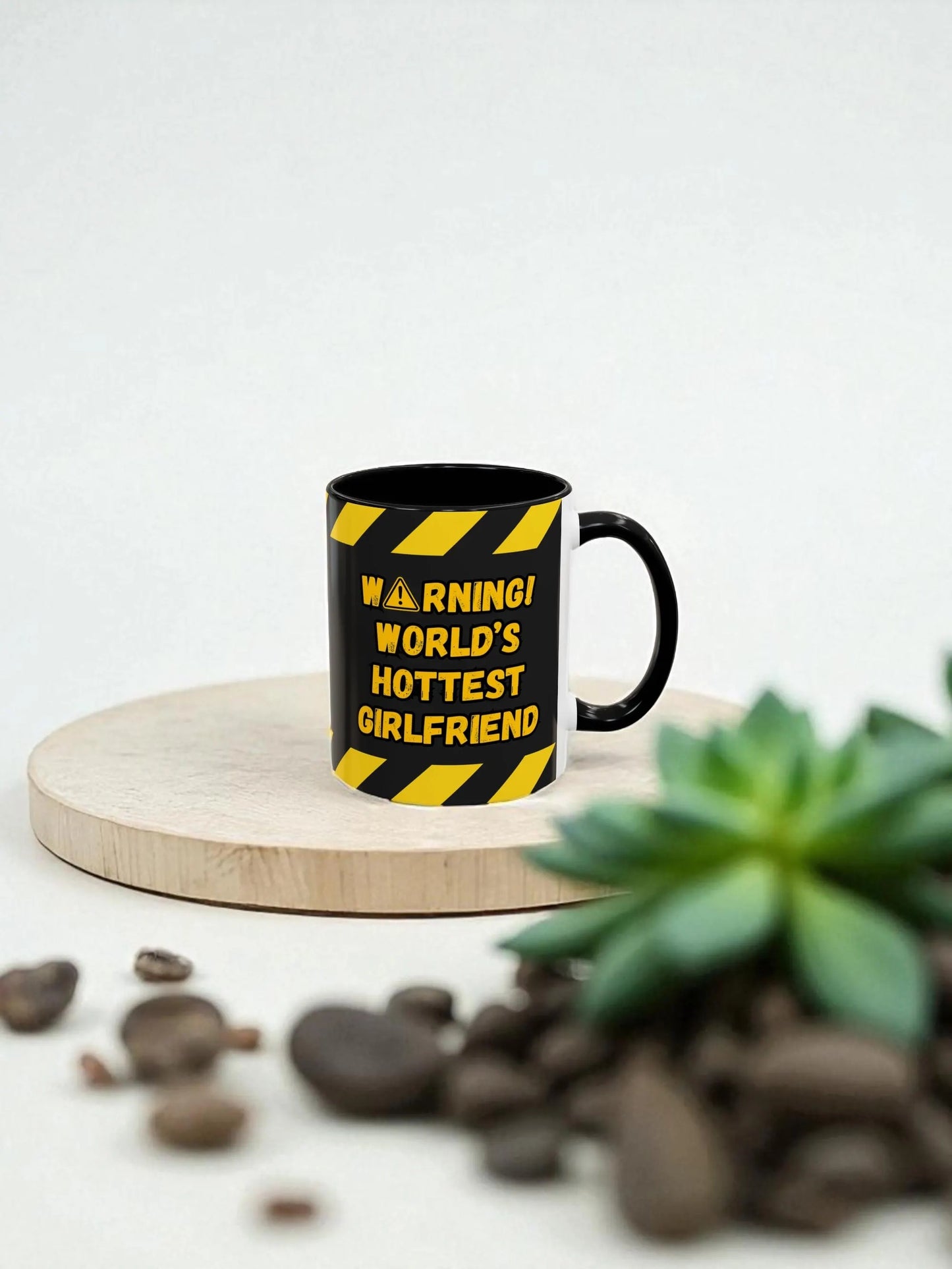 Black mug with yellow warning text on a wooden coaster with coffee beans and a plant.