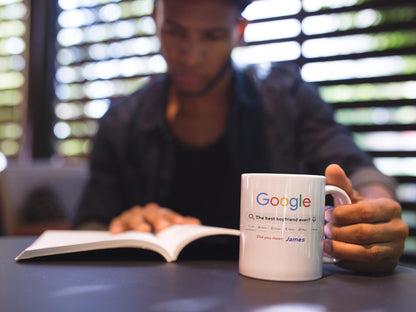 Person reading a book with a 'Google' mug on a table