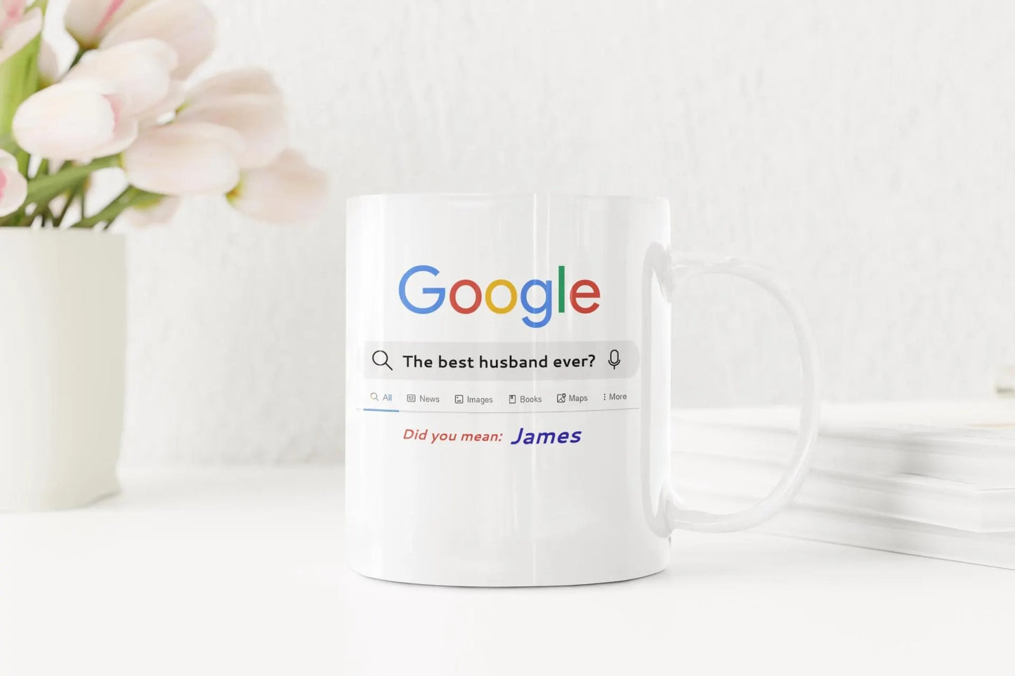 White mug with Google search query printed on it, next to a vase of flowers.