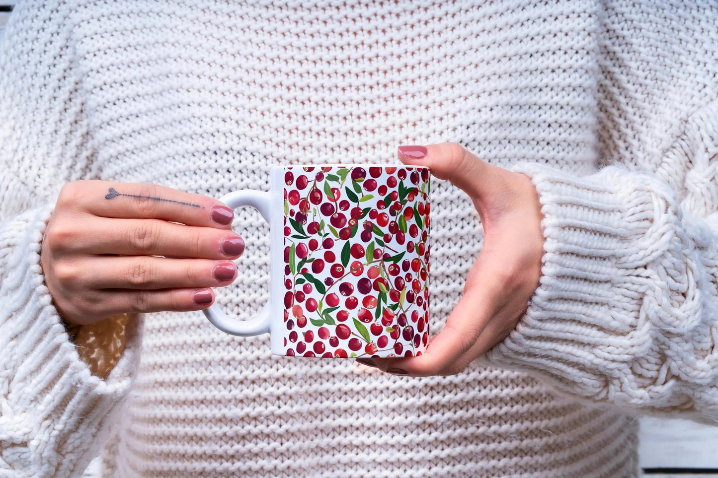 Person holding a mug with a cranberry pattern against a white sweater background