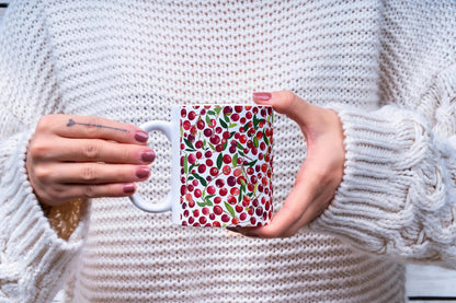 Person holding a mug with a cranberry pattern against a white sweater background