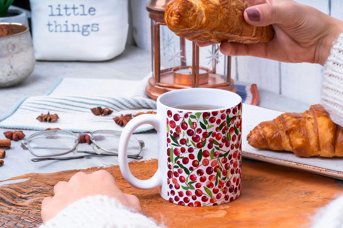 Person holding a cranberry patterned mug with croissants on a table