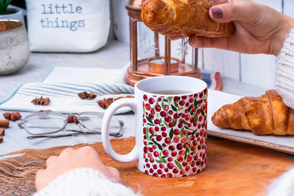Person holding a cranberry patterned mug with croissants on a table