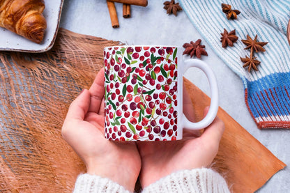 Hand holding a mug with a cranberry pattern on a wooden surface with cinnamon sticks and star anise.