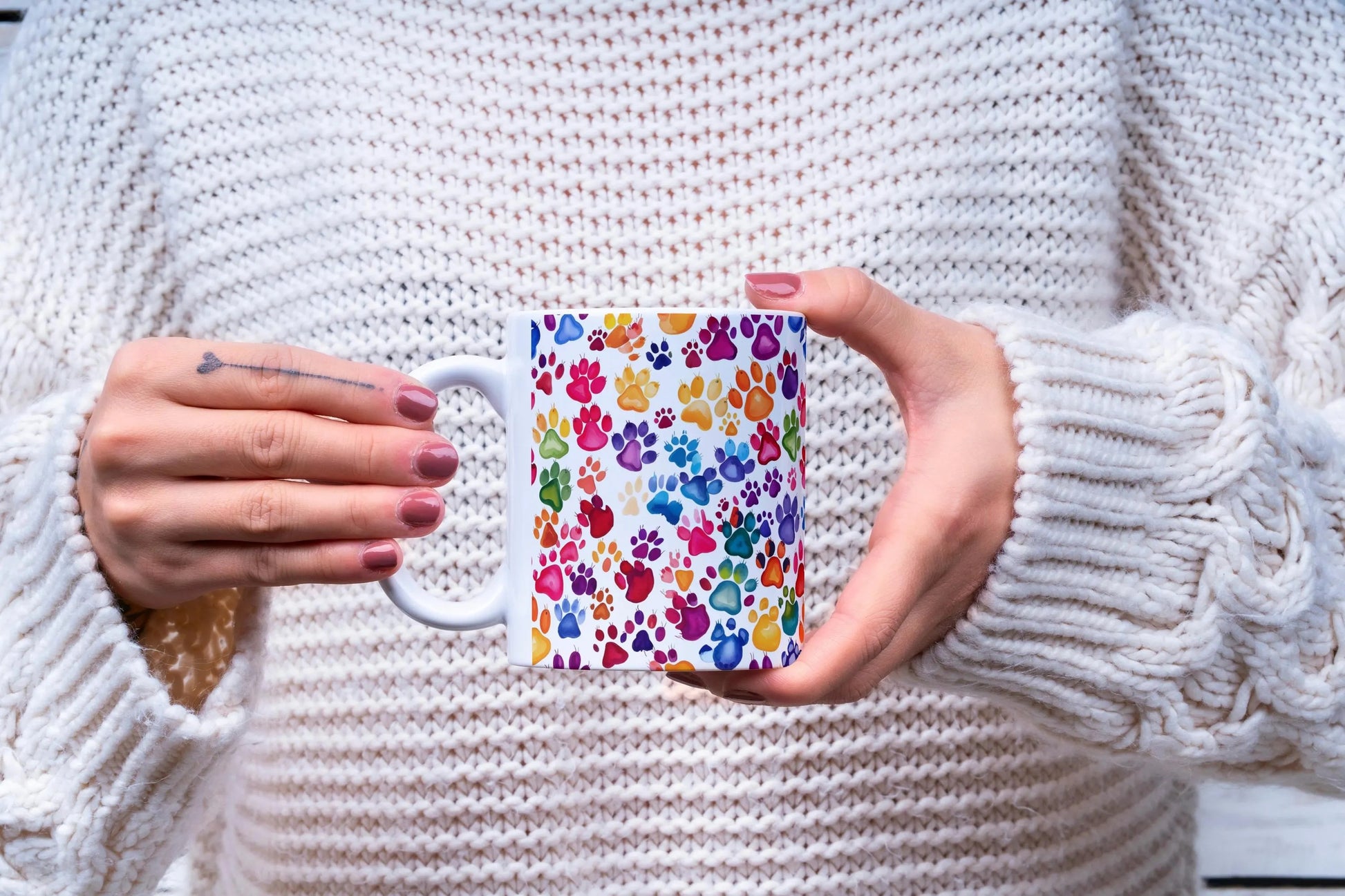 Person holding a mug with a colorful paw print design