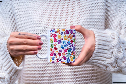 Person holding a mug with a colorful paw print design