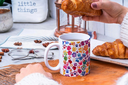Colorful mug with paw prints on a table with pastries and glasses.