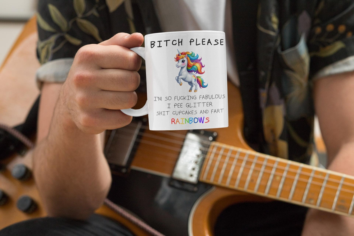 Person holding a mug with a humorous design and text, sitting next to a guitar.