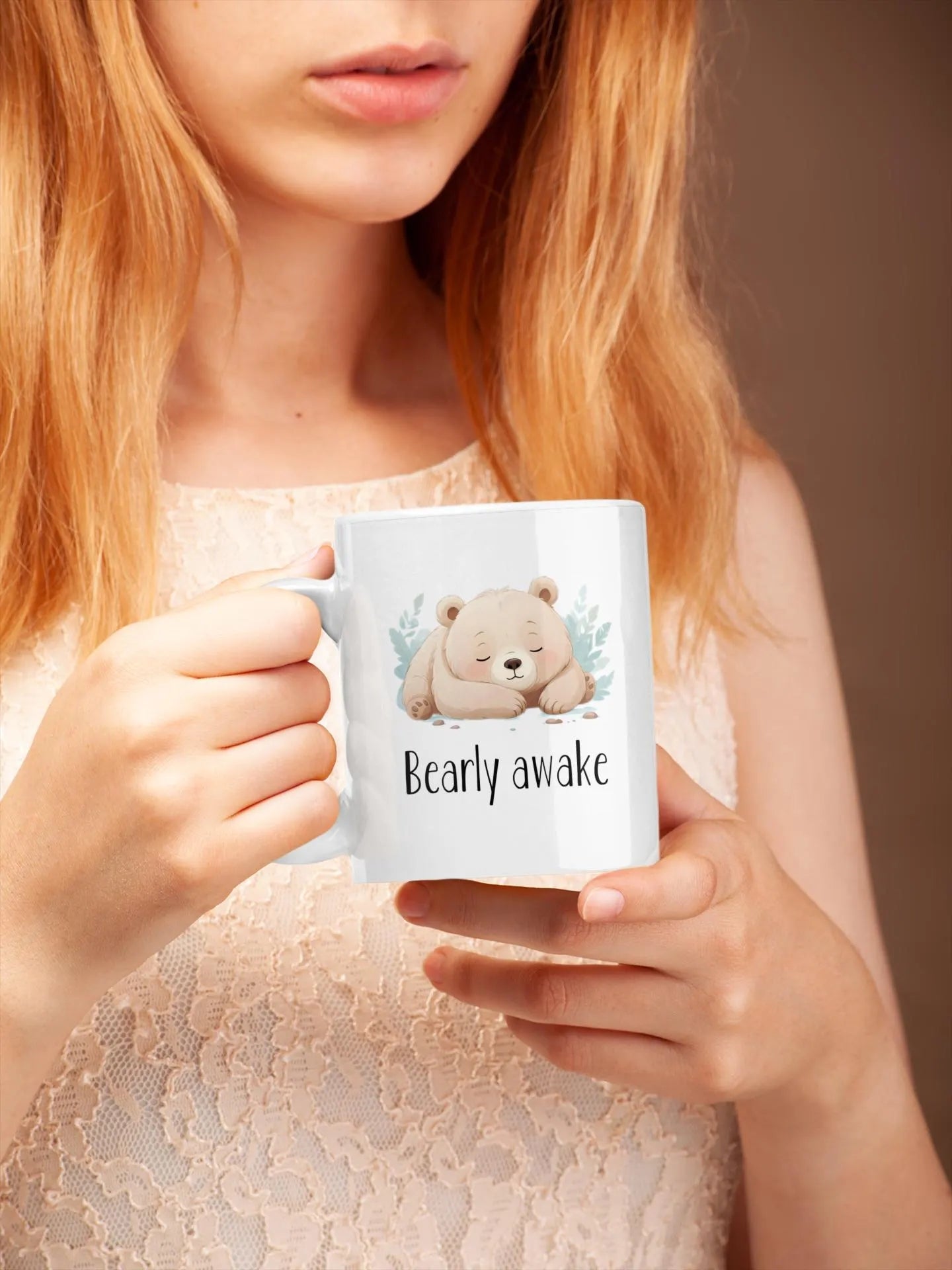 Person holding a mug with a bear illustration and text 'Bearly awake' against a plain background