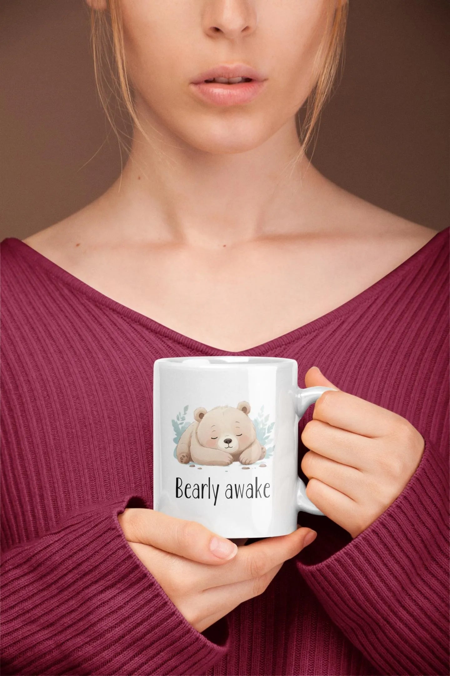 Person holding a mug with a bear illustration and text, against a plain background
