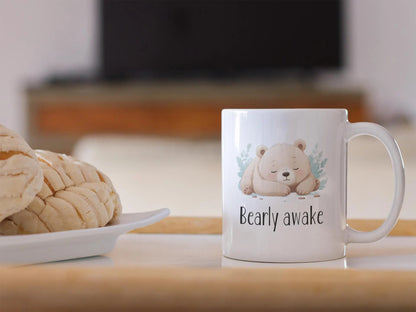 Mug with a bear design and 'Bearly awake' text on a table with cookies.