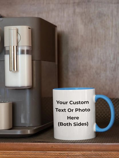 White mug with blue handle on a wooden surface next to a coffee machine.